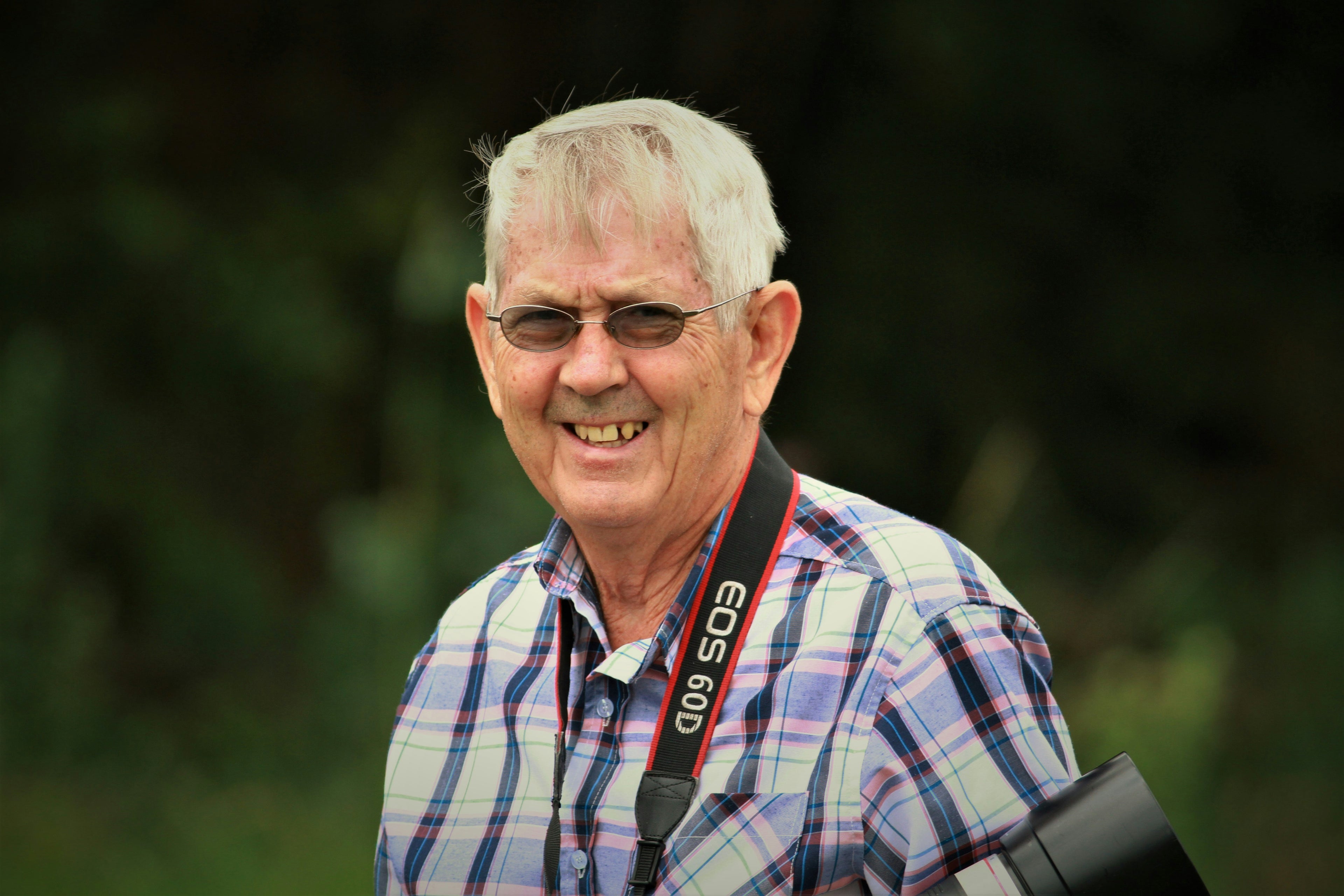 Man with white hair and glasses holding a camera, standing outdoors with a blurred natural background review for Beyond This Stones QR code memorial for headstones